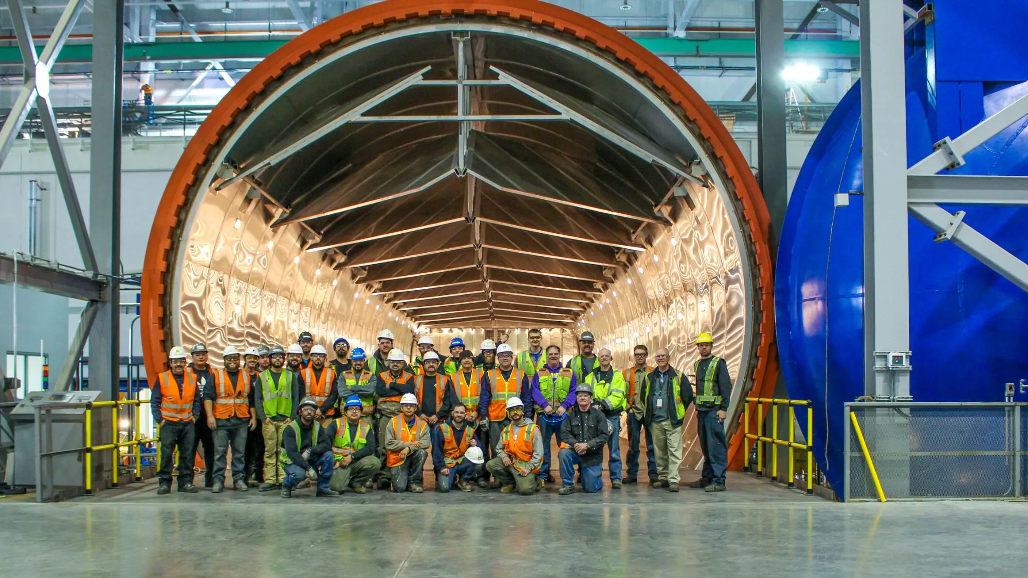 An ASC crew in hard hats and safety vests standing at the open door of a large composite autoclave