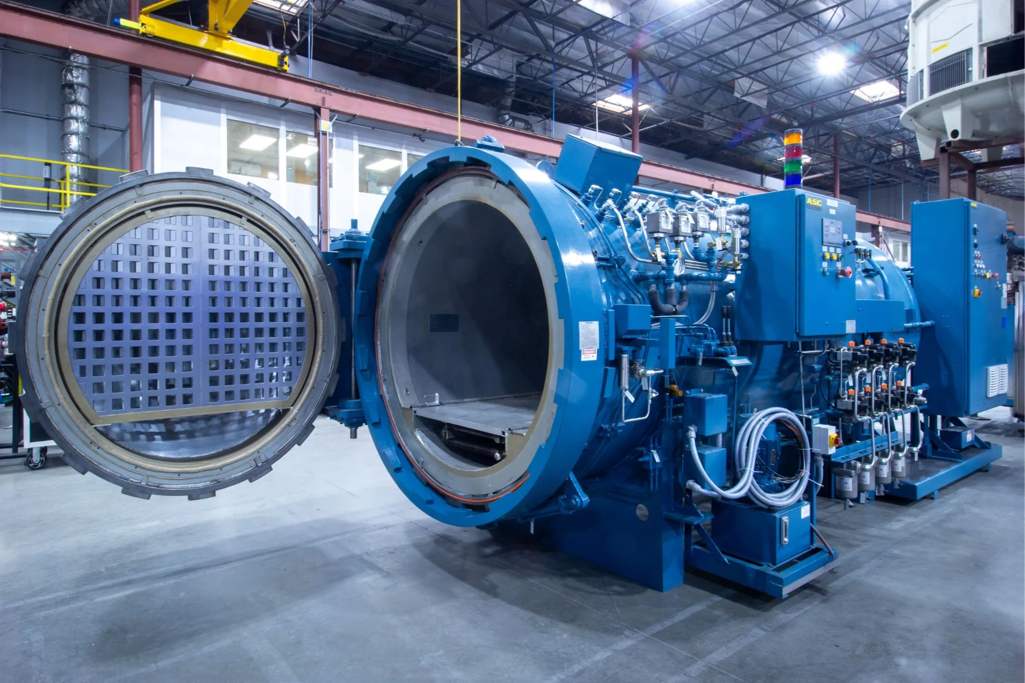 A blue ASC Econoclave with its door swung open, showing the insulated interior, load rails, and the CPC control cabinet beside it