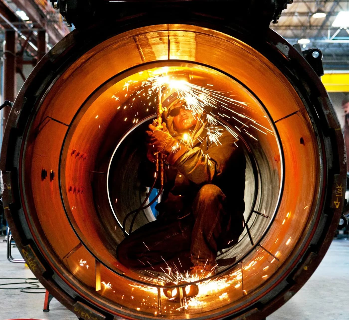 An ASC fabricator working with a torch inside a pressure vessel ring, sparks lighting the steel