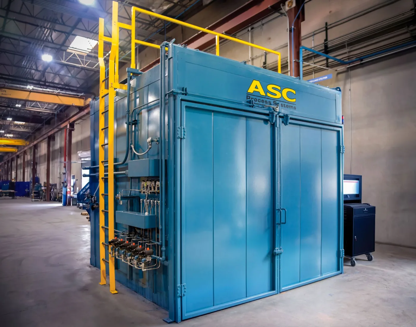 A blue ASC walk-in curing oven with double doors, a roof platform ladder, and its CPC control cabinet